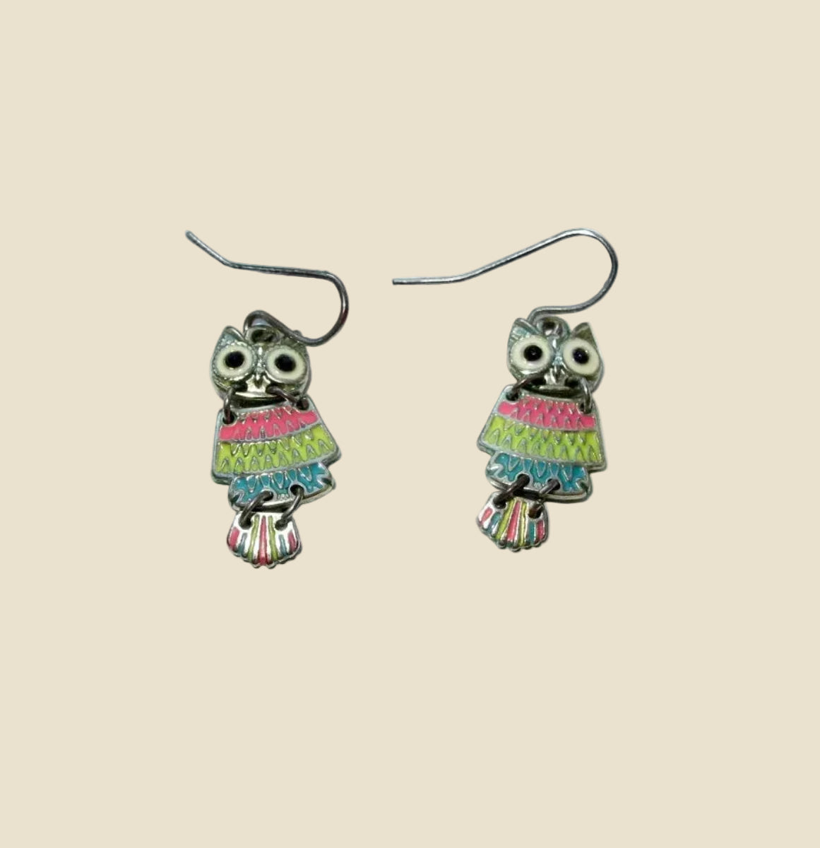 A pair of owl-shaped dangle earrings with colorful striped dresses and silver fishhook wires, displayed on a plain white surface.