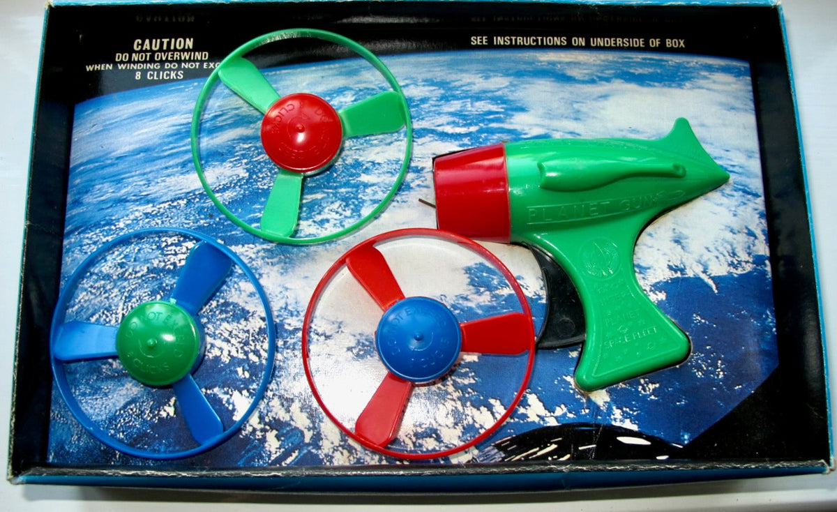 Vintage toy set in its original box, featuring a green toy blaster and three spinning propeller discs in green, blue, and red, printed on a space-themed background.