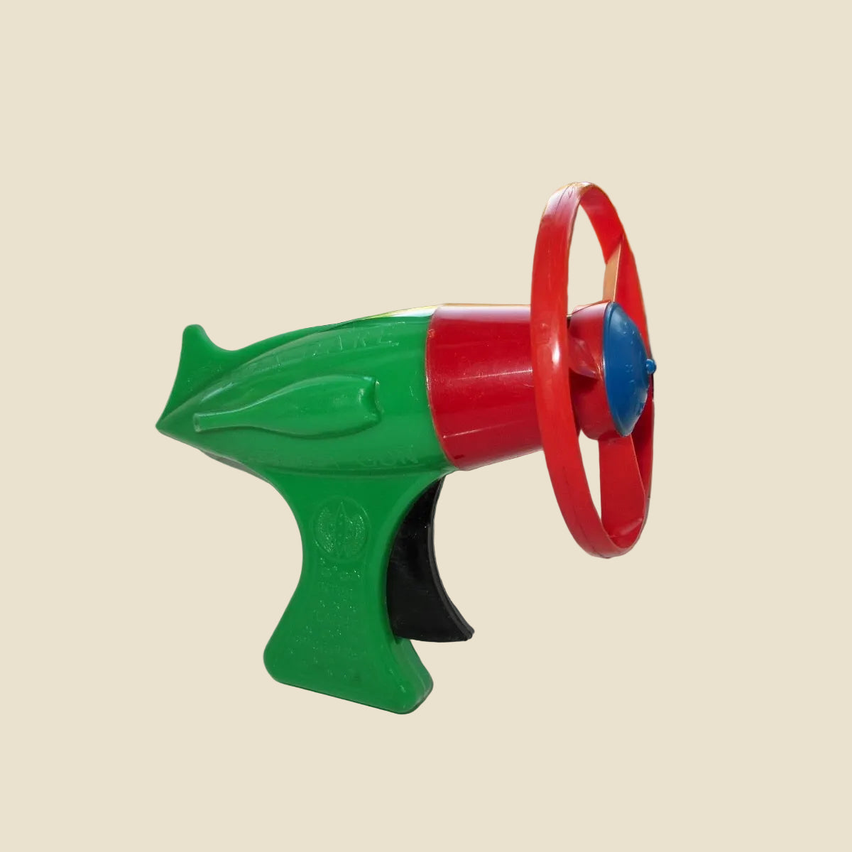 A colourful plastic toy blaster or toy gun with a green body, red barrel, and red wheel-like front detail,