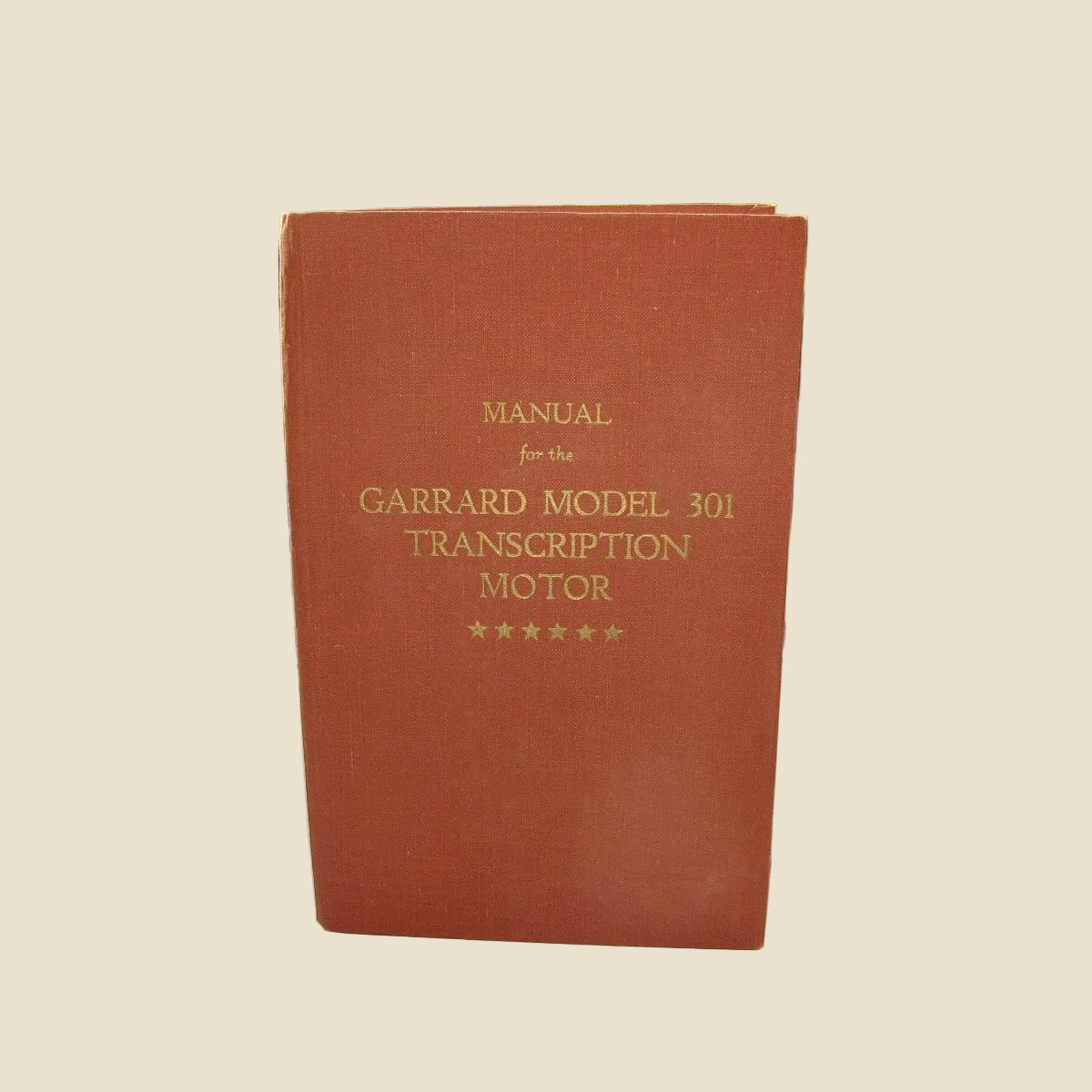 A red/brown hardcover manual standing upright, with gold text reading 'MANUAL for the GARRARD MODEL 301 TRANSCRIPTION MOTOR' and five stars at the bottom. 