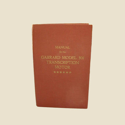 A red/brown hardcover manual standing upright, with gold text reading 'MANUAL for the GARRARD MODEL 301 TRANSCRIPTION MOTOR' and five stars at the bottom. 