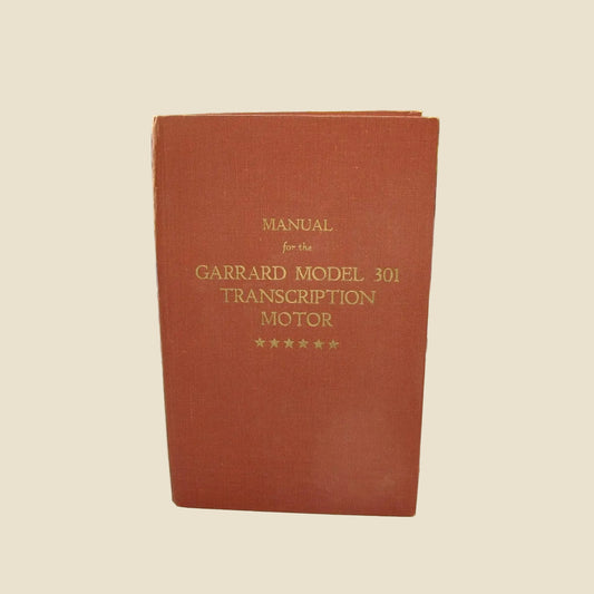 A red/brown hardcover manual standing upright, with gold text reading 'MANUAL for the GARRARD MODEL 301 TRANSCRIPTION MOTOR' and five stars at the bottom. 