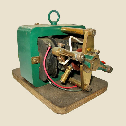 A vintage mechanical device with a painted green metal casing, brass-toned metal parts, and red and white wires, mounted on a wooden base.